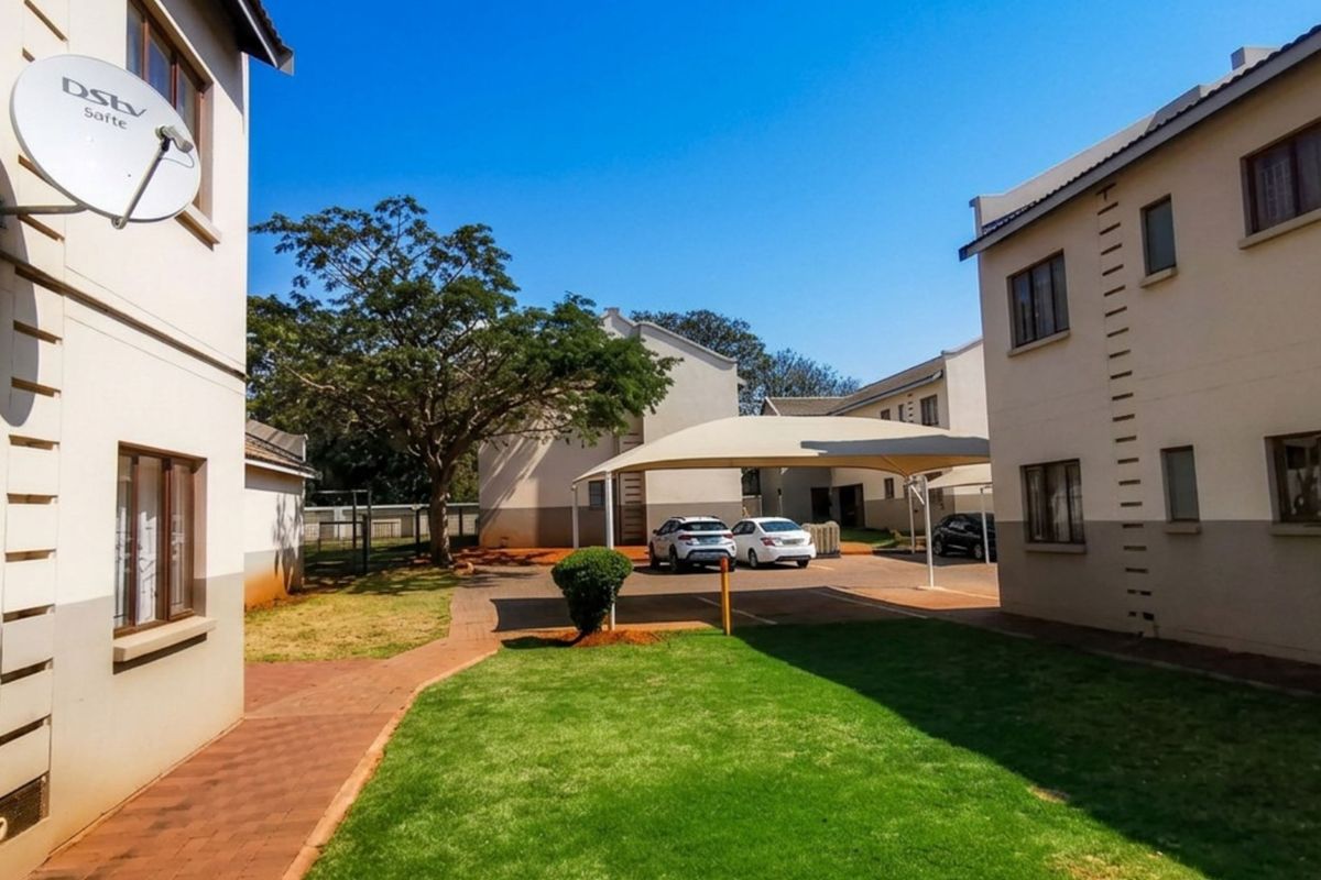 A view of the townhouse complex exterior featuring a shared lawn, paved walkways, and covered parking bays.