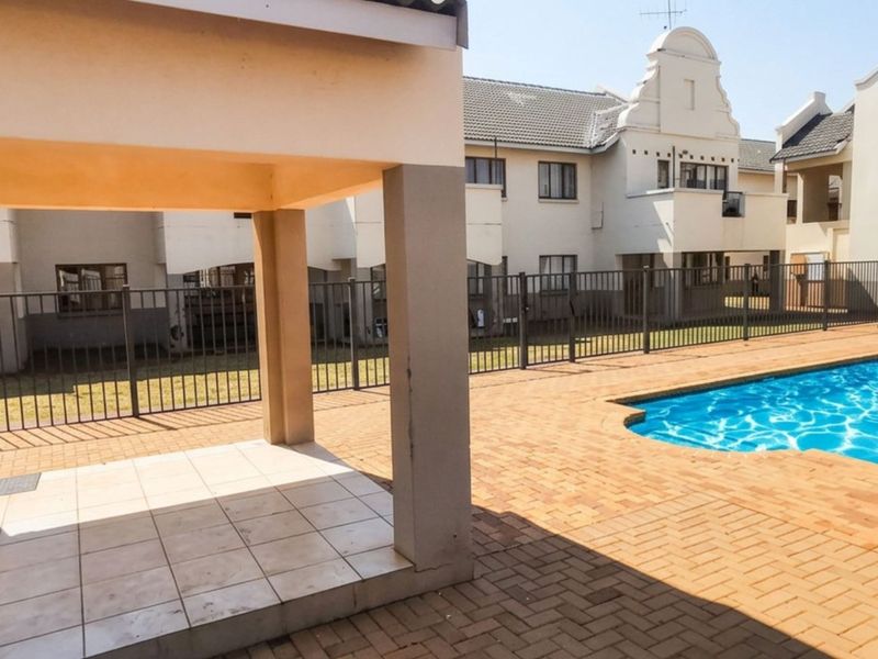 Communal pool area featuring a paved deck, covered gazebo, and secure metal perimeter fencing within the townhouse complex.