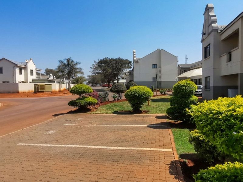 A view of the townhouse complex street, featuring paved parking bays, well-maintained landscaped gardens, and surrounding residential units.