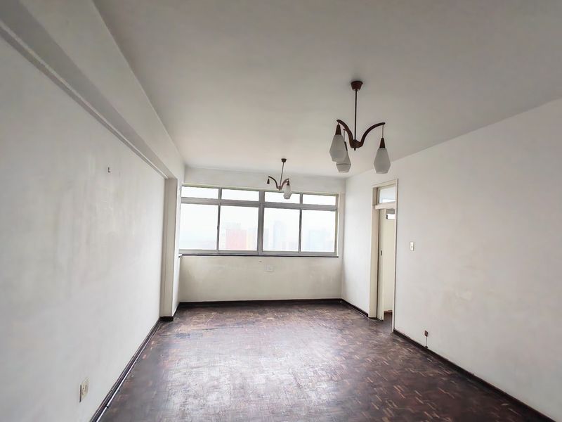 An empty living room featuring original parquet flooring, large aluminium-framed windows, and neutral wall finishes, offering a blank canvas for renovation.