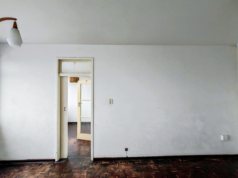 An empty living room featuring original parquet flooring, a classic transom door frame, and neutral wall finishes, offering a blank canvas for renovation.