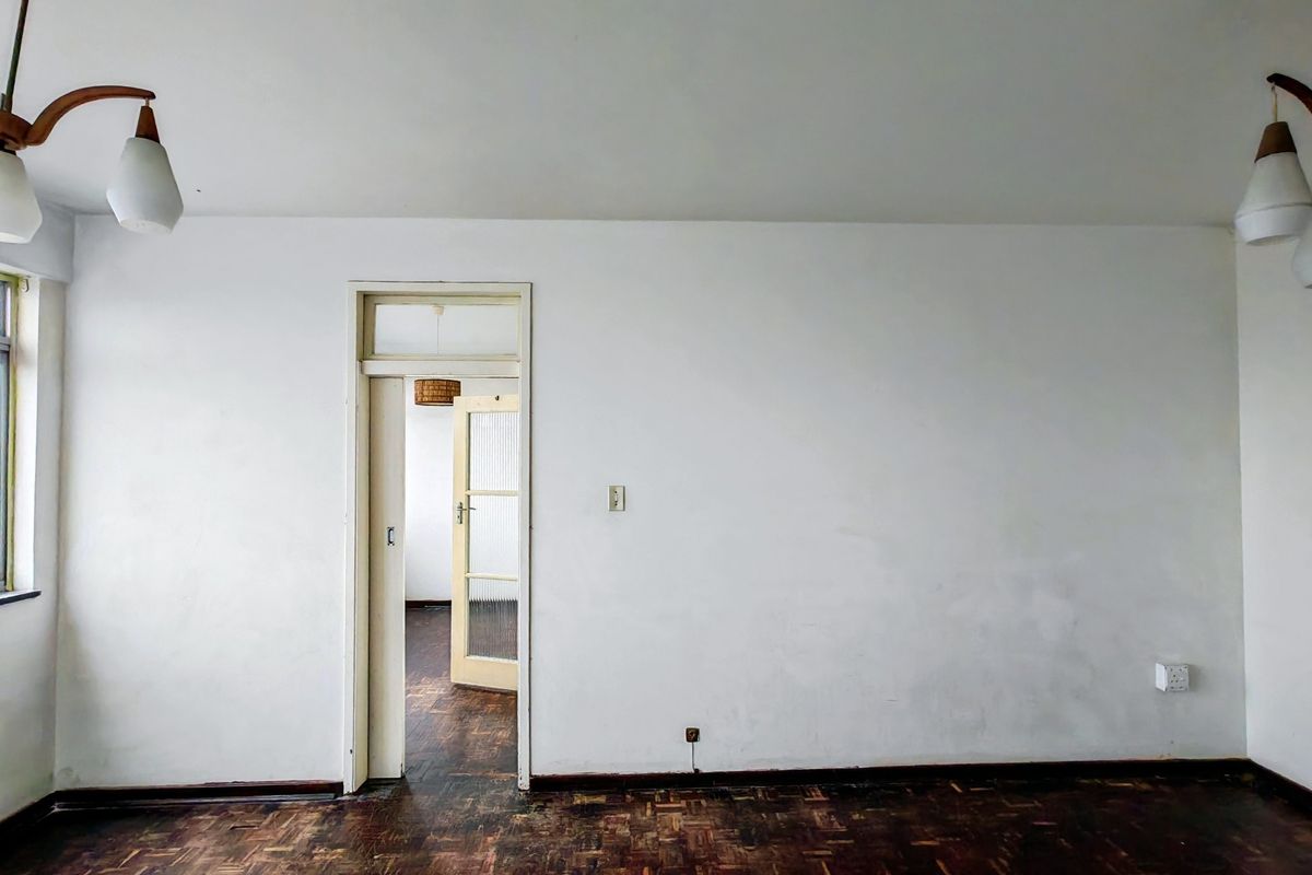 An empty living room featuring original parquet flooring, a classic transom door frame, and neutral wall finishes, offering a blank canvas for renovation.