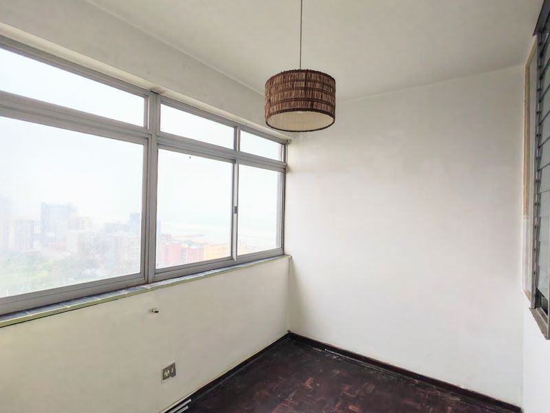 An enclosed balcony or sunroom featuring large aluminium windows, parquet flooring, and a neutral interior, offering potential as a bright study or relaxation area.
