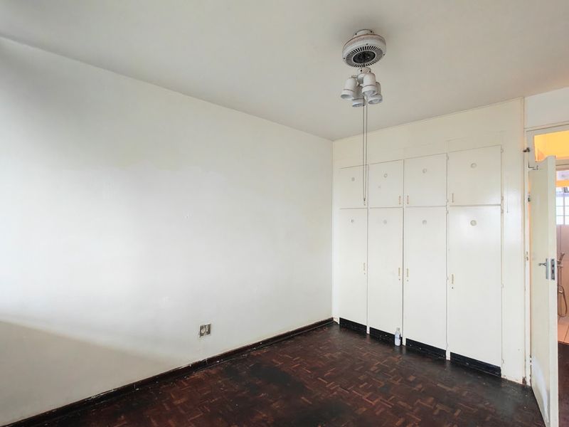 An empty bedroom featuring original parquet flooring, built-in storage cupboards, and a ceiling fan, with direct access to an adjoining bathroom.