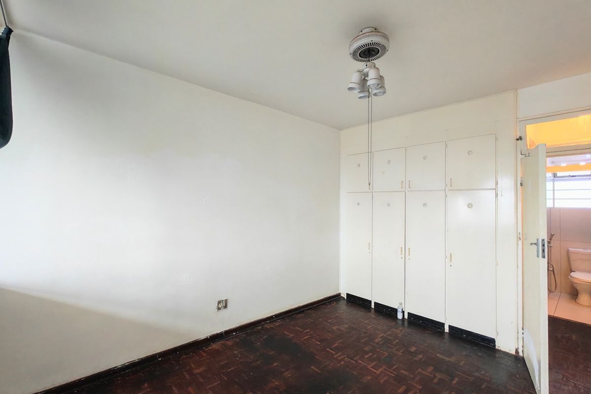 An empty bedroom featuring original parquet flooring, built-in storage cupboards, and a ceiling fan, with direct access to an adjoining bathroom.