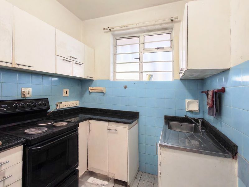 A compact kitchen featuring dated cabinetry, blue tiled backsplash, laminate countertops, and a functional electric stove, offering significant potential for modern renovation.