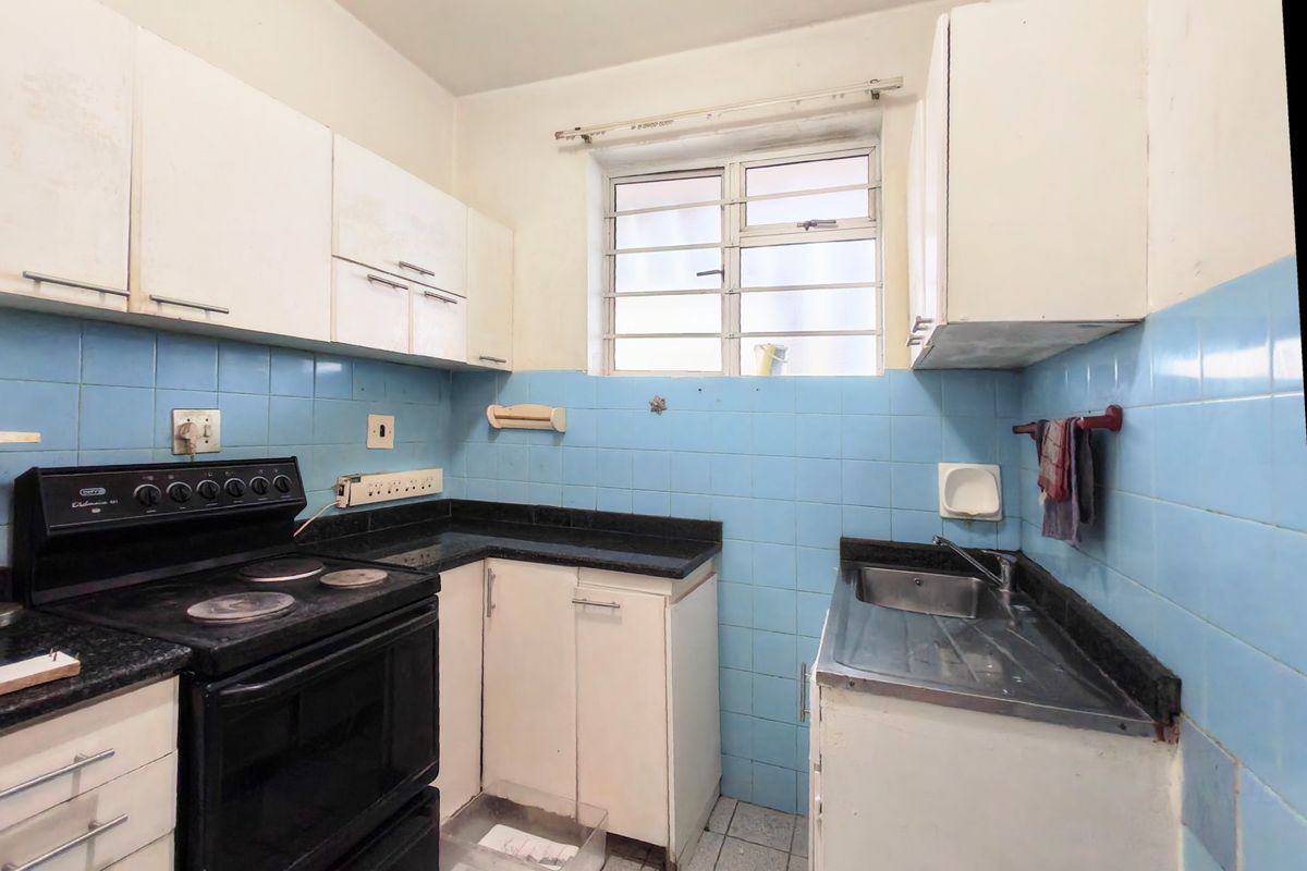 A compact kitchen featuring dated cabinetry, blue tiled backsplash, laminate countertops, and a functional electric stove, offering significant potential for modern renovation.