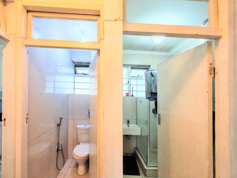 A functional bathroom featuring a separate toilet area and a shower enclosure with tiled finishes and wall-mounted basin.