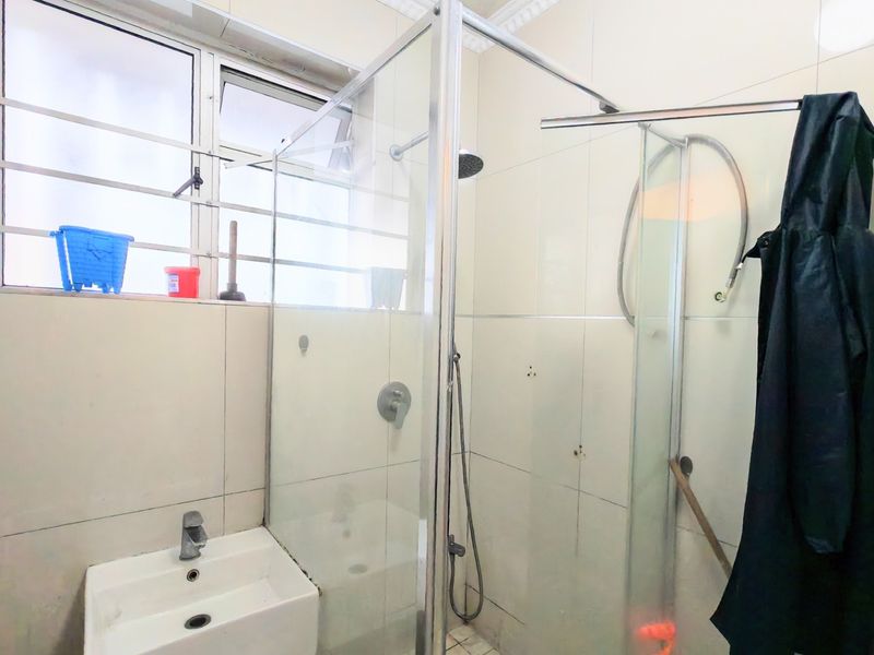 A functional bathroom featuring a glass shower enclosure, wall-mounted basin, and tiled walls, requiring some maintenance and cosmetic updates.