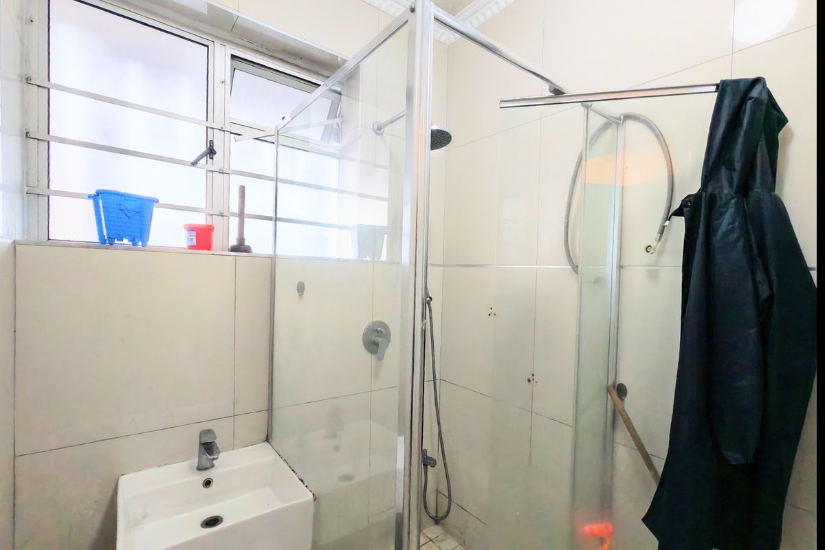 A functional bathroom featuring a glass shower enclosure, wall-mounted basin, and tiled walls, requiring some maintenance and cosmetic updates.