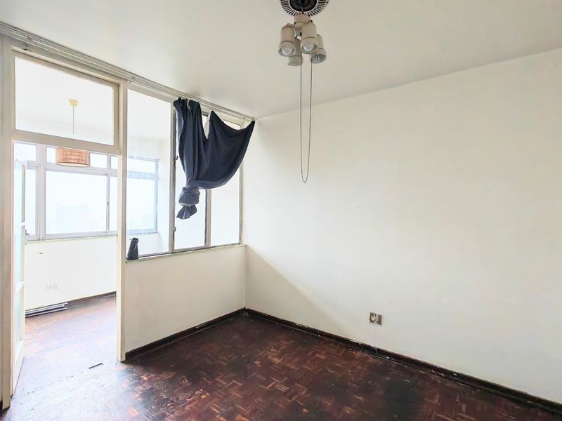 An empty living area featuring original parquet flooring, an internal glass partition, and access to an enclosed balcony space.