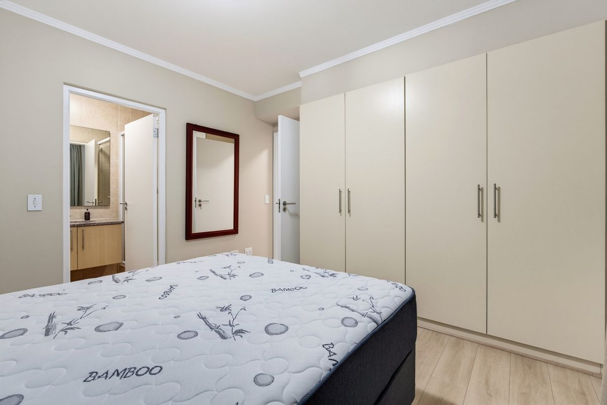 A well-maintained bedroom featuring neutral walls, laminate flooring, and ample built-in cupboard storage, with direct access to an en-suite bathroom.