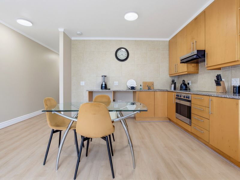 Open-plan kitchen and dining area featuring light wood cabinetry, granite countertops, built-in oven, and modern laminate flooring.