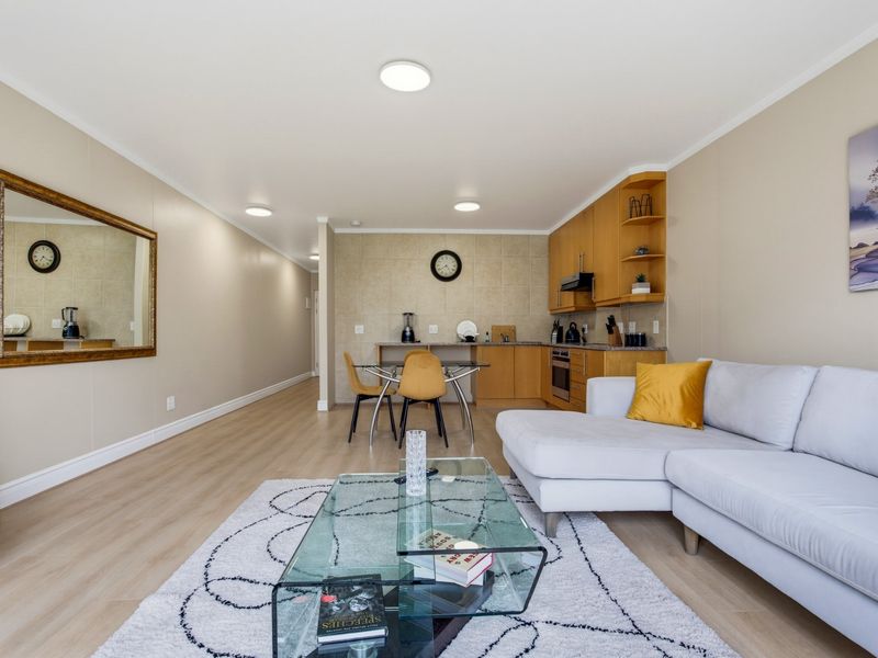 An open-plan living and kitchen area featuring light laminate flooring, neutral walls, and functional built-in cabinetry with a tiled backsplash.