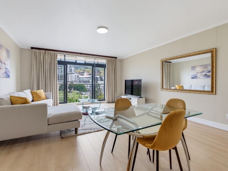 Bright open-plan living and dining area featuring modern laminate flooring and large sliding glass doors leading to a balcony with urban views.