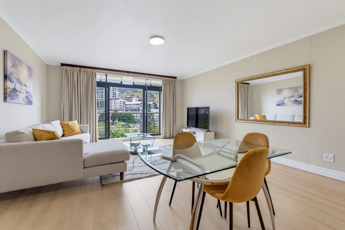 Bright open-plan living and dining area featuring modern laminate flooring and large sliding glass doors leading to a balcony with urban views.