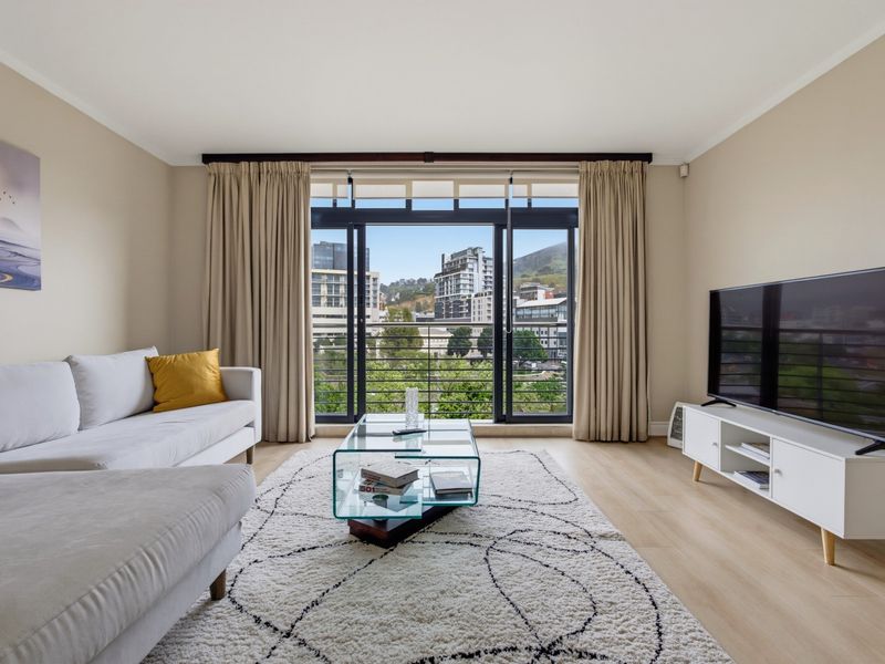 A bright and well-maintained living room featuring laminate flooring and large sliding glass doors that open to an urban view.