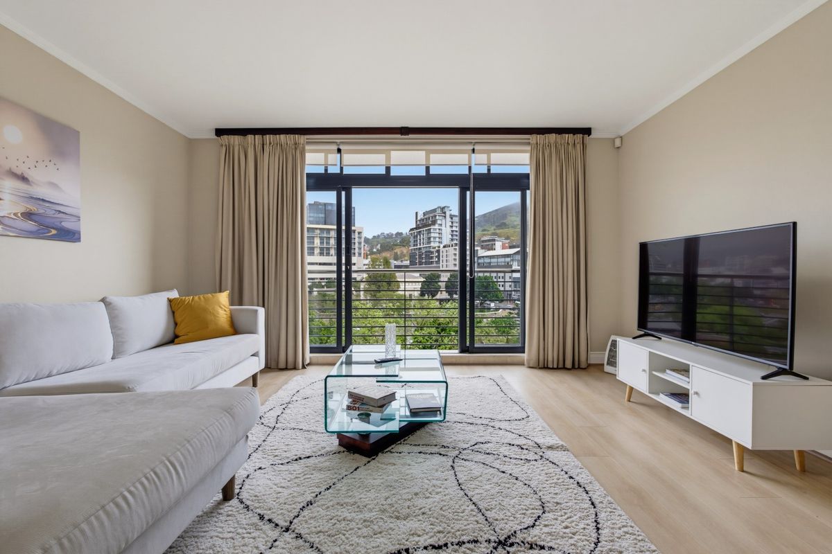 A bright and well-maintained living room featuring laminate flooring and large sliding glass doors that open to an urban view.