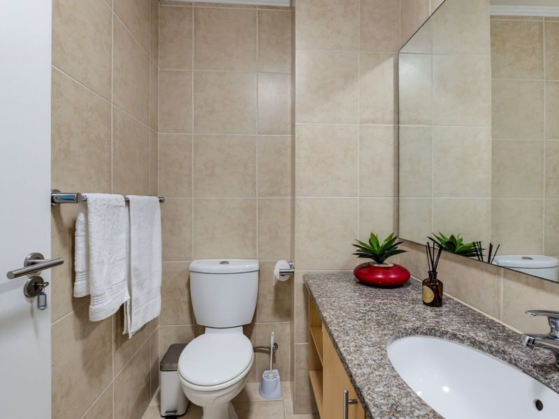 A compact bathroom featuring neutral wall tiles, a granite-topped vanity with an integrated sink, and a large wall-mounted mirror.