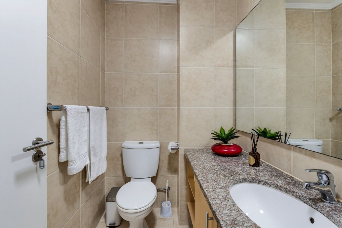 A compact bathroom featuring neutral wall tiles, a granite-topped vanity with an integrated sink, and a large wall-mounted mirror.