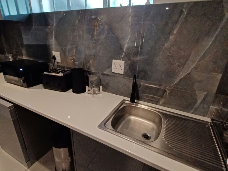 Modern kitchen area featuring a clean stone countertop, stainless steel sink with black tap, and elegant marble-effect splashback tiling.