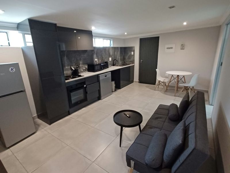 Modern open-plan living area featuring a sleek kitchen with dark cabinetry, integrated appliances, and neutral tiled flooring throughout the combined space.