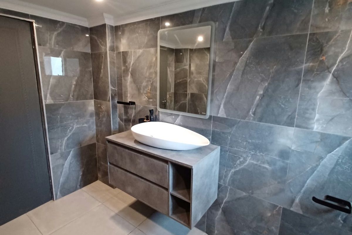 Modern bathroom featuring a floating vanity with a vessel sink, complemented by large-format dark marble-effect wall tiles and neutral floor tiling.