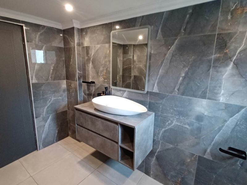Modern bathroom featuring a floating vanity with a vessel sink, complemented by large-format dark marble-effect wall tiles and neutral floor tiling.
