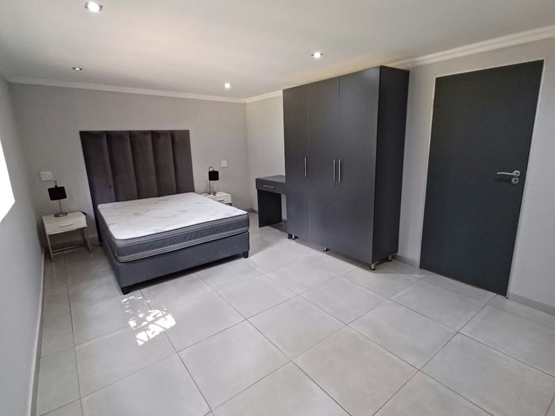 A spacious bedroom featuring modern tiled flooring, recessed downlighting, and a built-in wardrobe, offering a clean and neutral living space.
