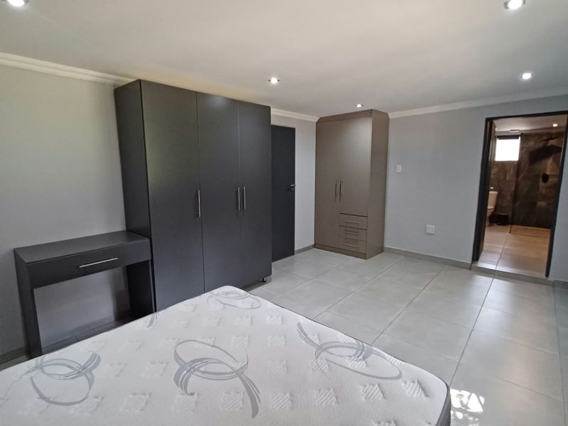Spacious bedroom featuring neutral tiled flooring, recessed downlighting, and ample built-in cupboard storage, with direct access to an en-suite bathroom.