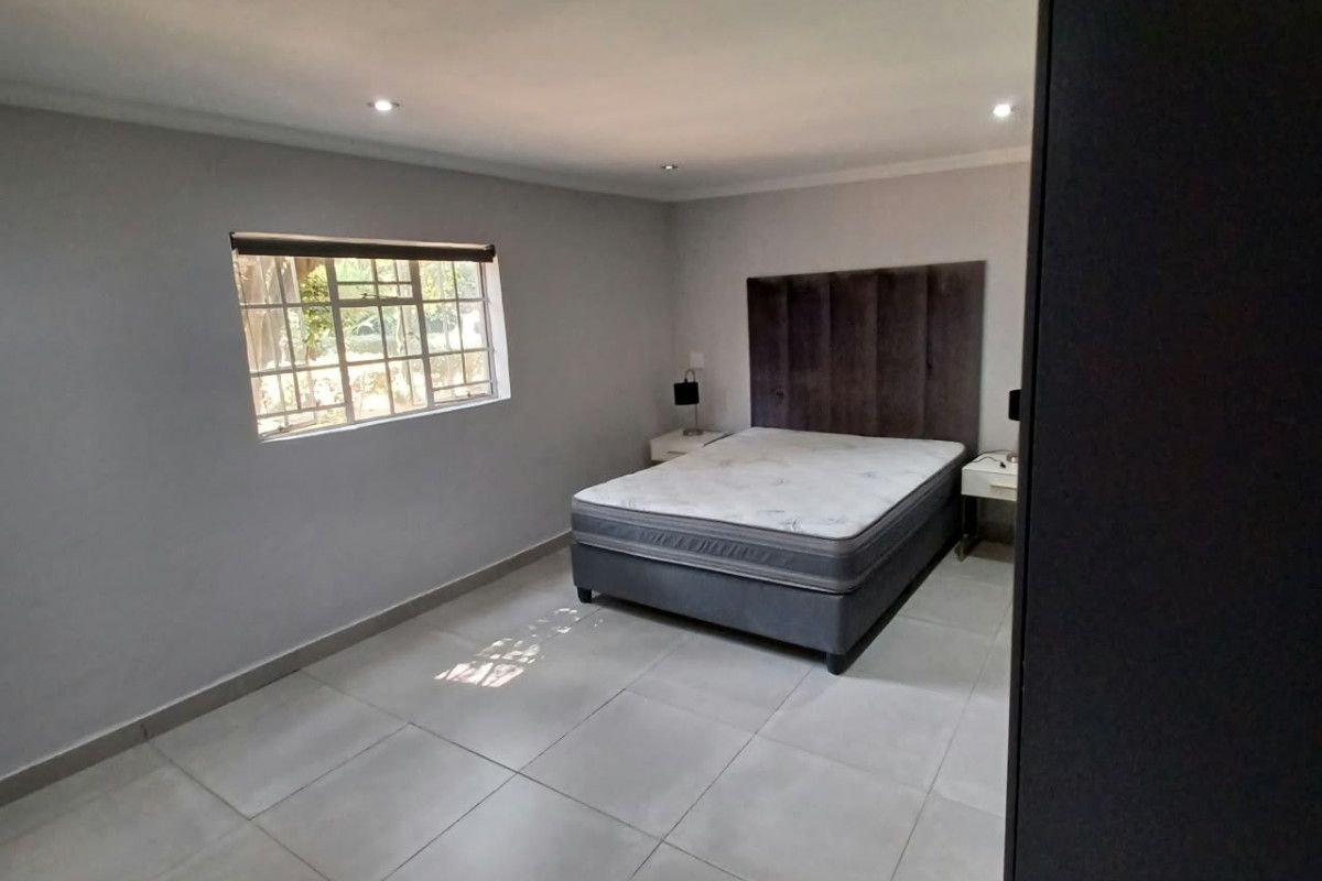 A spacious bedroom featuring neutral tiled flooring, recessed downlighting, and a window fitted with security burglar bars.