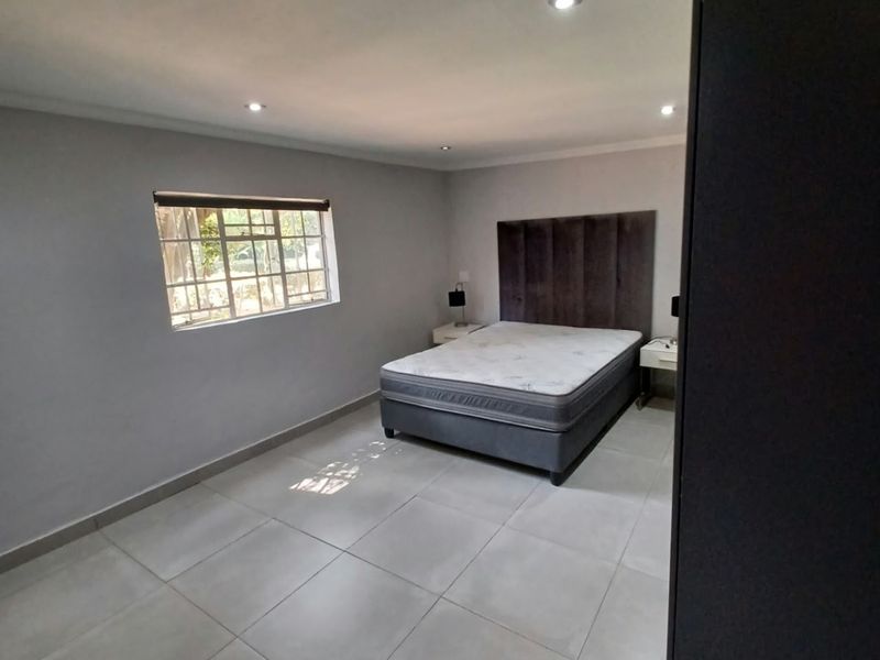 A spacious bedroom featuring neutral tiled flooring, recessed downlighting, and a window fitted with security burglar bars.