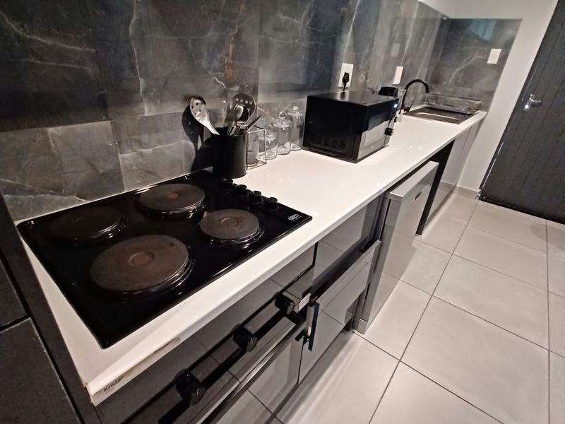 Modern kitchen featuring dark cabinetry, stone countertops, a sleek tiled backsplash, and integrated electric cooking appliances with tiled flooring.