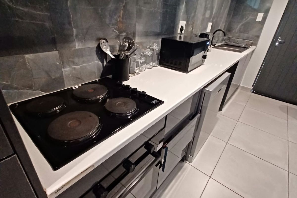 Modern kitchen featuring dark cabinetry, stone countertops, a sleek tiled backsplash, and integrated electric cooking appliances with tiled flooring.