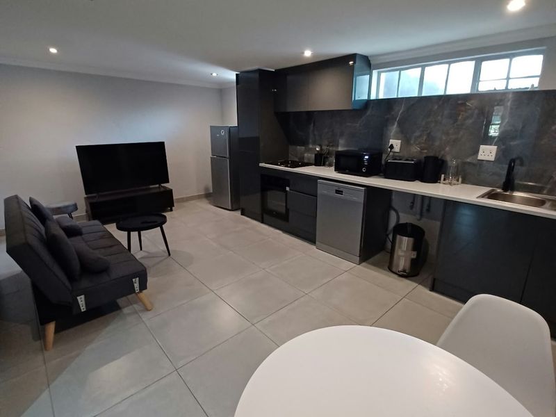 Modern open-plan living area featuring a sleek kitchen with dark cabinetry, stone countertops, integrated appliances, and large format floor tiles.