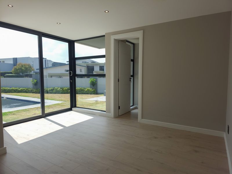 A bright, modern living area featuring light laminate flooring, recessed downlights, and expansive aluminium sliding doors with views of the garden and pool.