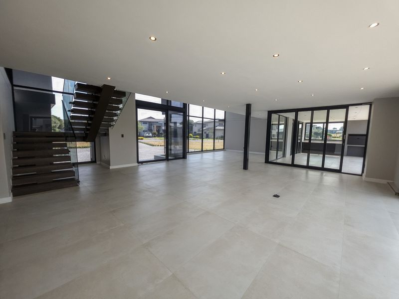 Spacious open-plan living area featuring large floor-to-ceiling windows, modern tiled flooring, and a striking floating staircase with glass balustrades.