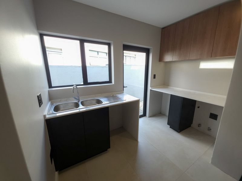 A clean, modern scullery featuring double sinks, stone countertops, ample built-in cabinetry, and direct access to an outdoor area.