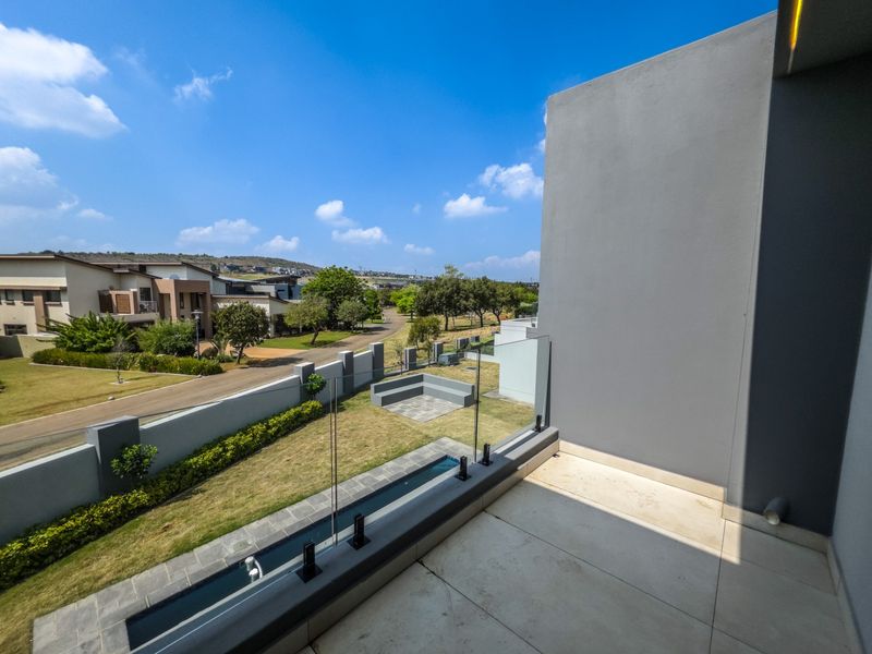 Modern balcony featuring a sleek glass balustrade and tiled flooring, offering elevated views over the estate and surrounding landscape.