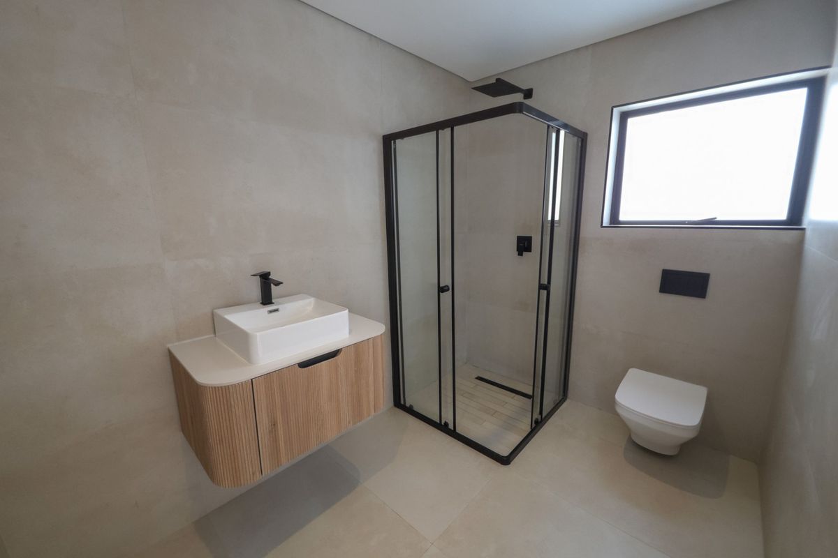 Modern bathroom featuring a wall-mounted vanity with vessel sink, corner shower enclosure with black fixtures, and a wall-hung toilet with neutral large-format tiling.