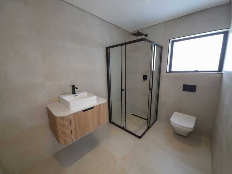 Modern bathroom featuring a wall-mounted vanity with vessel sink, corner shower enclosure with black fixtures, and a wall-hung toilet with neutral large-format tiling.
