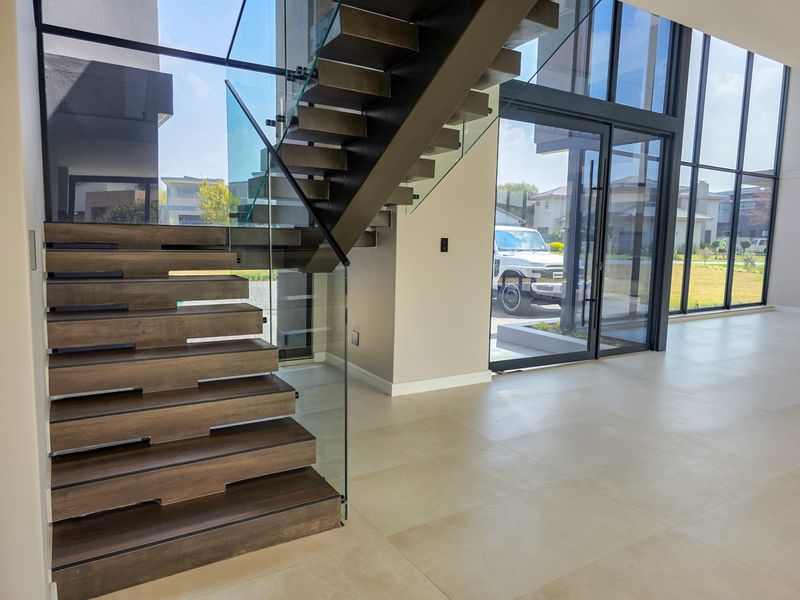 Modern entrance hall featuring a striking floating staircase with glass balustrades, large format floor tiles, and expansive floor-to-ceiling windows.