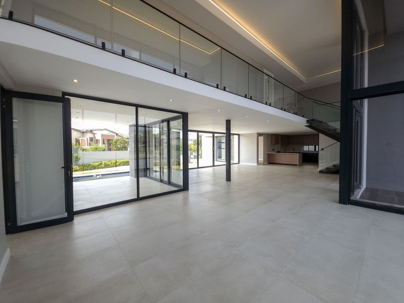 Spacious open-plan living area featuring large format floor tiles, a modern glass balustrade, and seamless indoor-outdoor flow through expansive sliding glass doors.