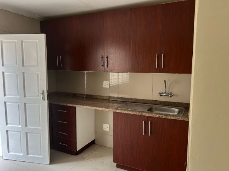 A functional kitchen area featuring dark wood cabinetry, granite countertops, a stainless steel sink, and tiled backsplash, offering a clean and practical workspace.