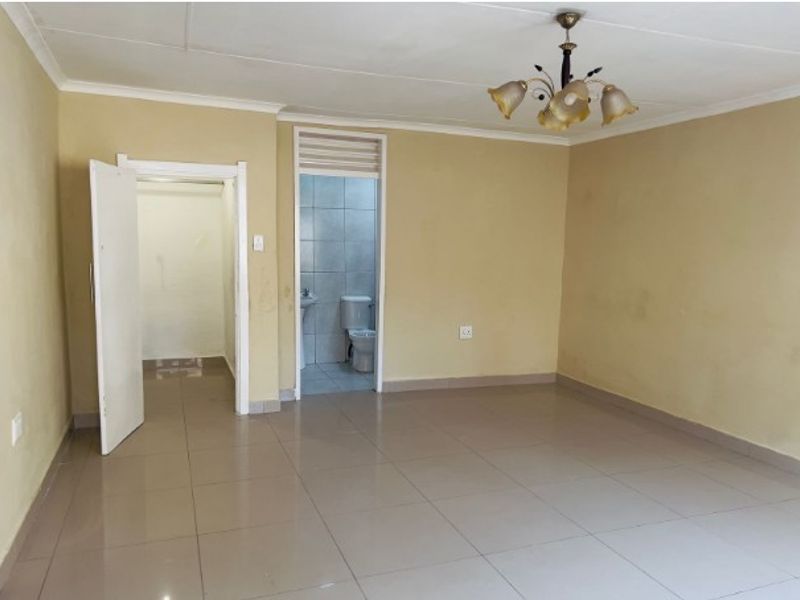 An empty bedroom featuring tiled flooring, a ceiling light fixture, and direct access to an en-suite bathroom and walk-in closet area.