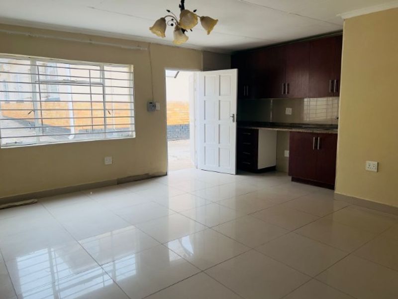 Open-plan living area featuring tiled flooring, built-in kitchen cabinetry with granite countertops, and direct access to the exterior.