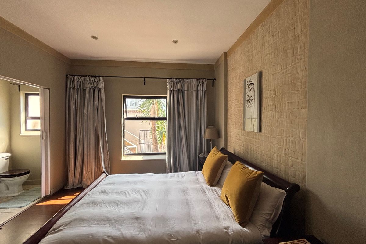 A well-maintained bedroom featuring a textured brick accent wall, recessed lighting, and direct access to an en-suite bathroom.
