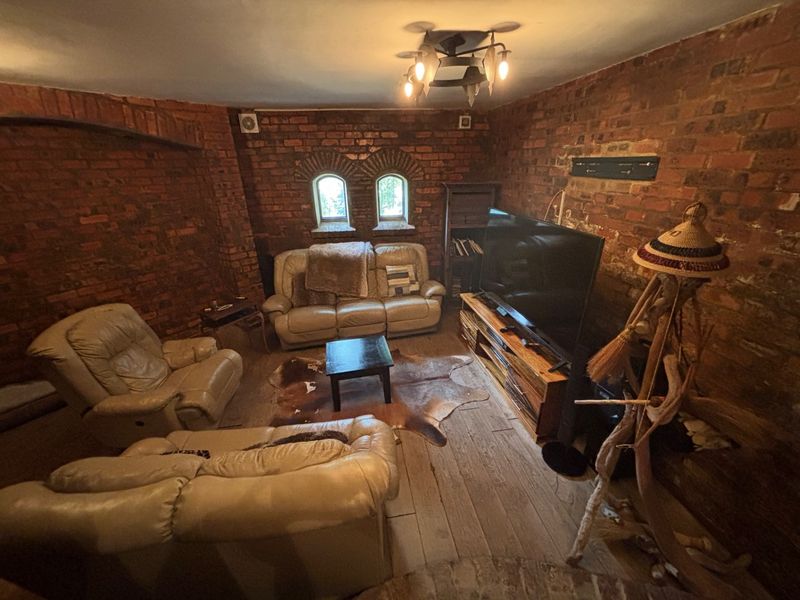 A rustic living room featuring exposed brick walls, arched windows, and timber flooring, creating a warm and character-filled atmosphere.