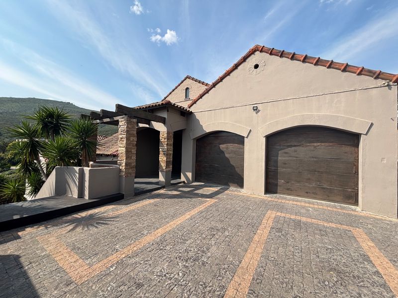 Front elevation of the property featuring a double garage, stone-clad pillars, a timber pergola, and a well-maintained paved driveway.