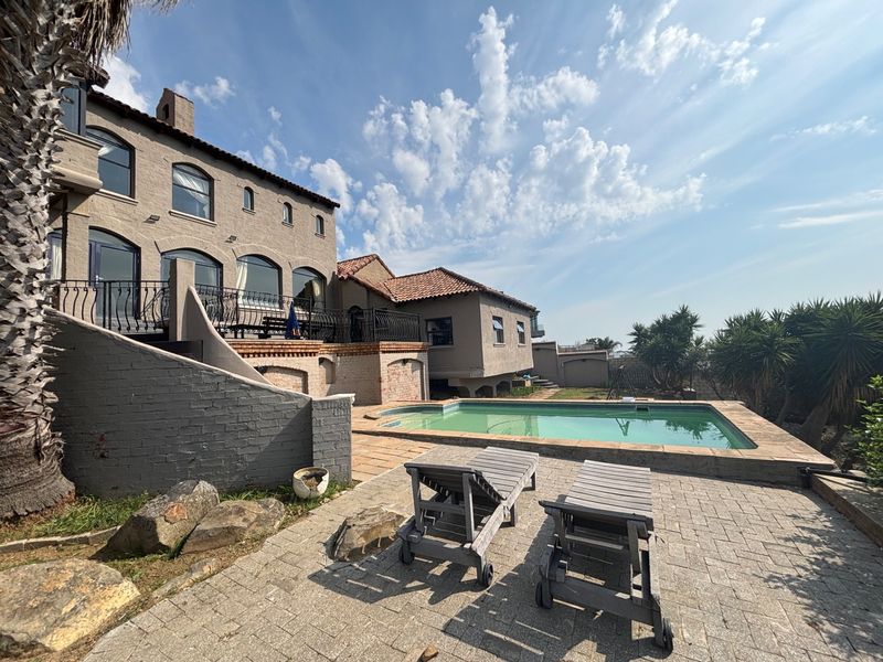 Rear exterior view featuring a swimming pool, paved patio area, and multi-story brick residence with arched windows and a balcony.